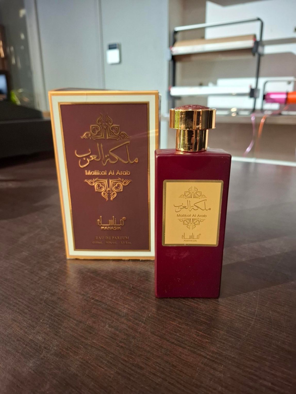 Rode parfumfles met gouden etiket naast een bijpassende bordeauxrode en gouden doos op een tafel.