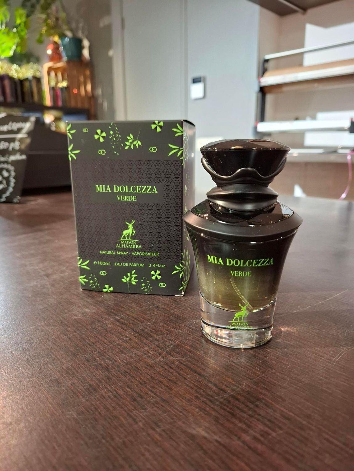 Zwarte parfumfles en -doos met groene accenten op een houten tafel.