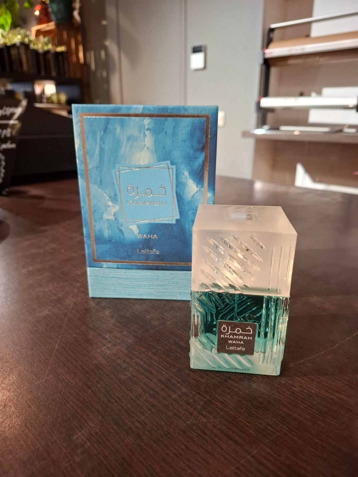 Twee blauwgroene parfumdoosjes op een houten tafel, een groter doosje achter een kleiner, flesvormig doosje.