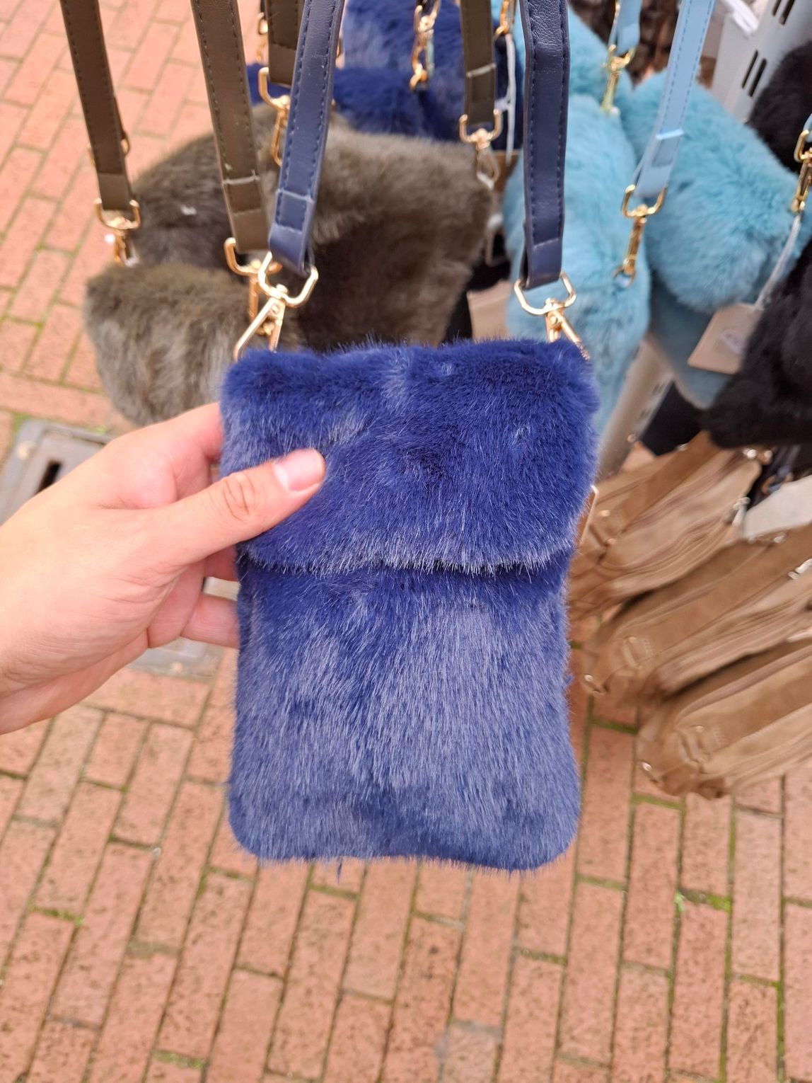 Hand die een blauwe, pluizige tas vasthoudt voor hangende handtassen op een openluchtmarkt.