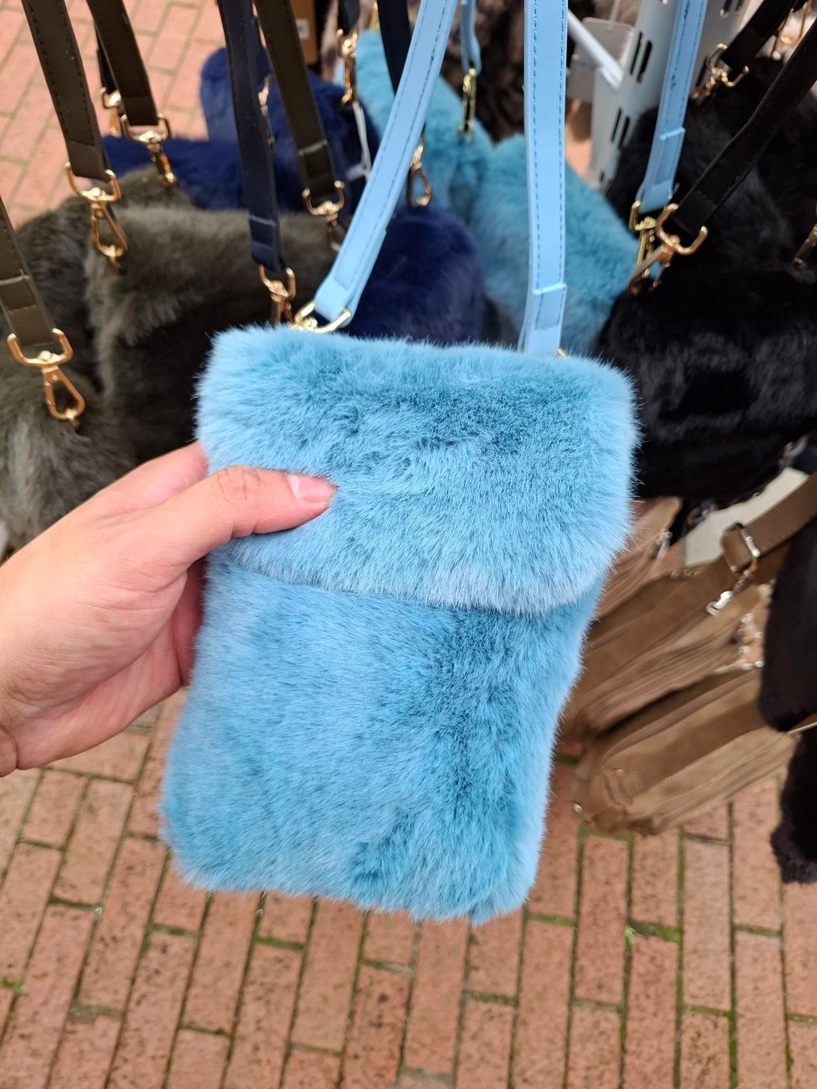 Hand die een pluizige lichtblauwe schoudertas vasthoudt voor hangende tassen buiten.