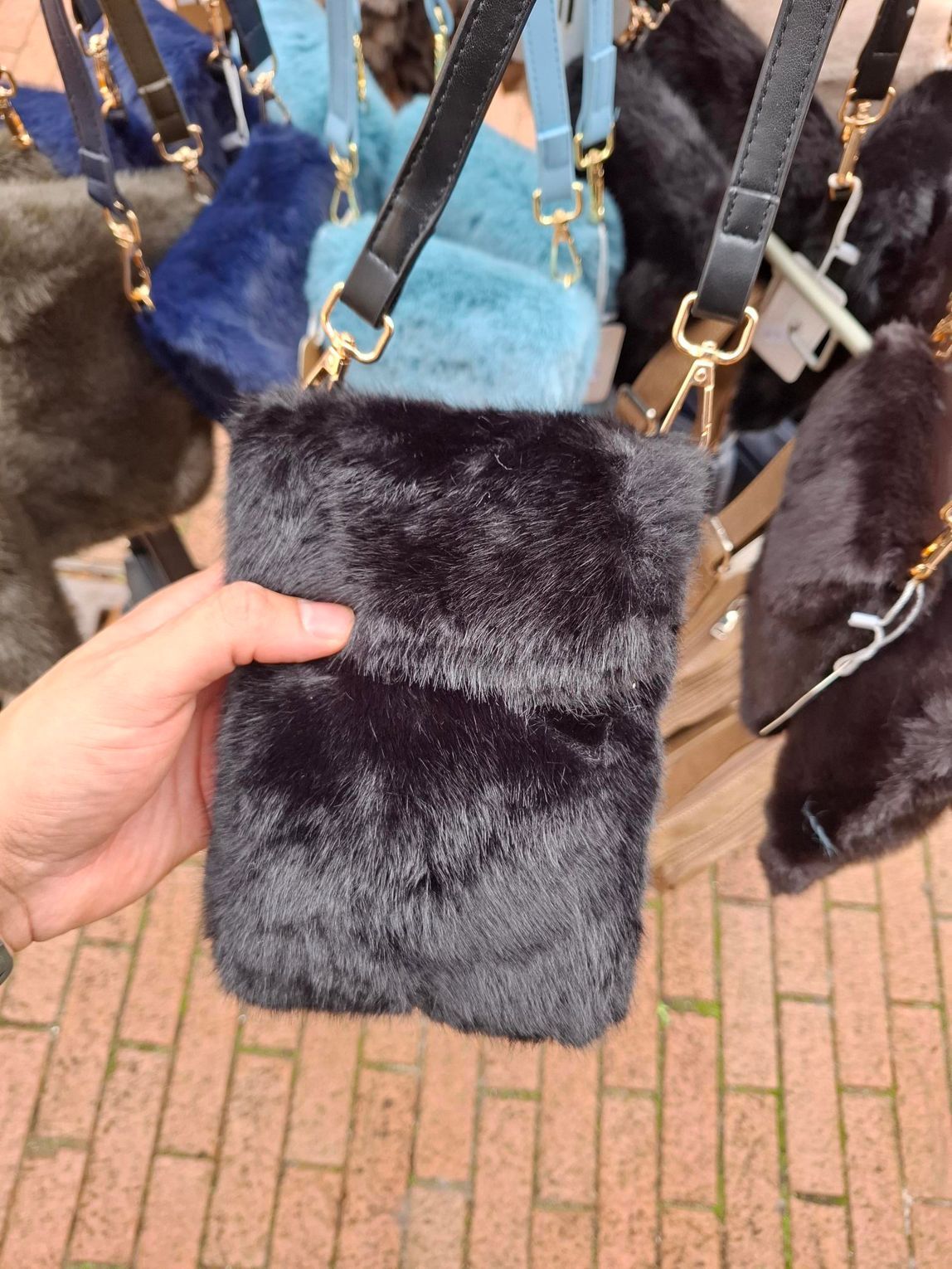 Hand die een zwarte tas van imitatiebont met een kettingriem vasthoudt bij een kraam op een buitenmarkt.