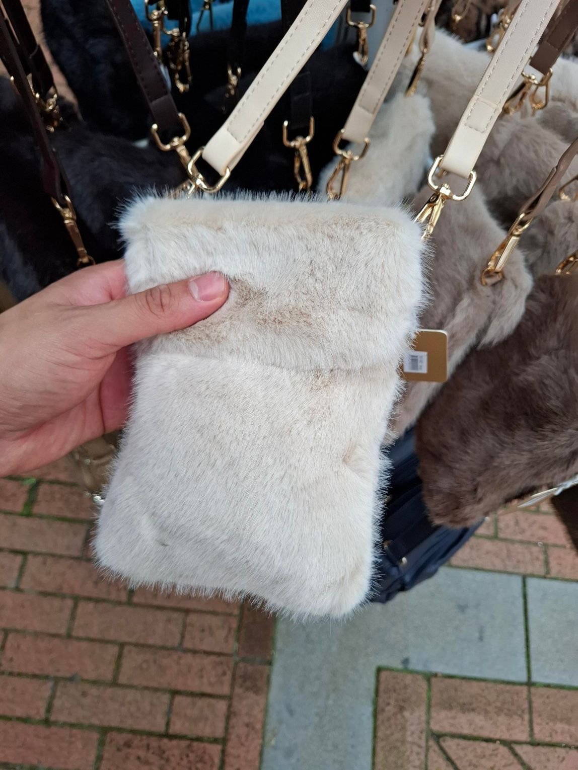 Hand die een pluizig wit buideltje vasthoudt voor hangende tassen op een bakstenen pad buiten.