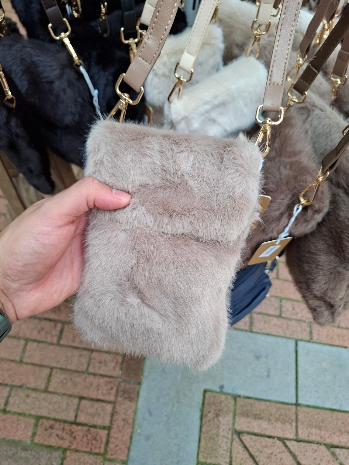 Hand die een lichtgrijze handtas van imitatiebont met gouden kettingriemen vasthoudt, buiten.