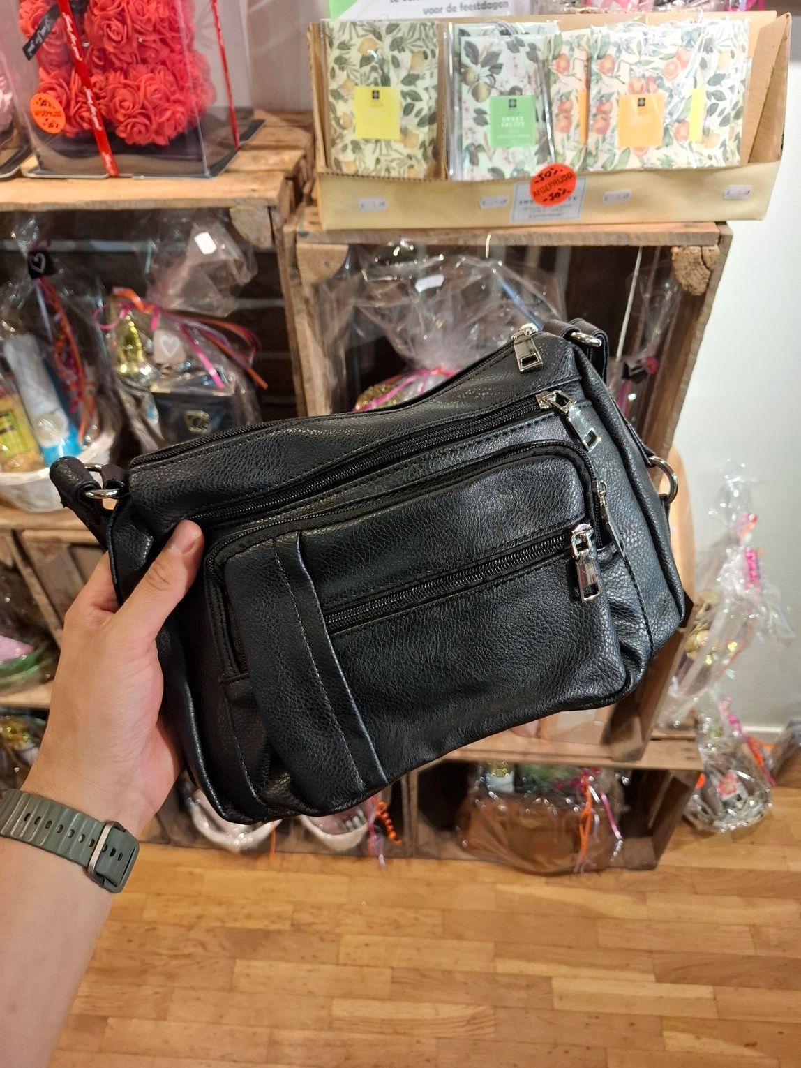 Hand die een zwarte leren schoudertas vasthoudt voor schappen met verpakte accessoires.