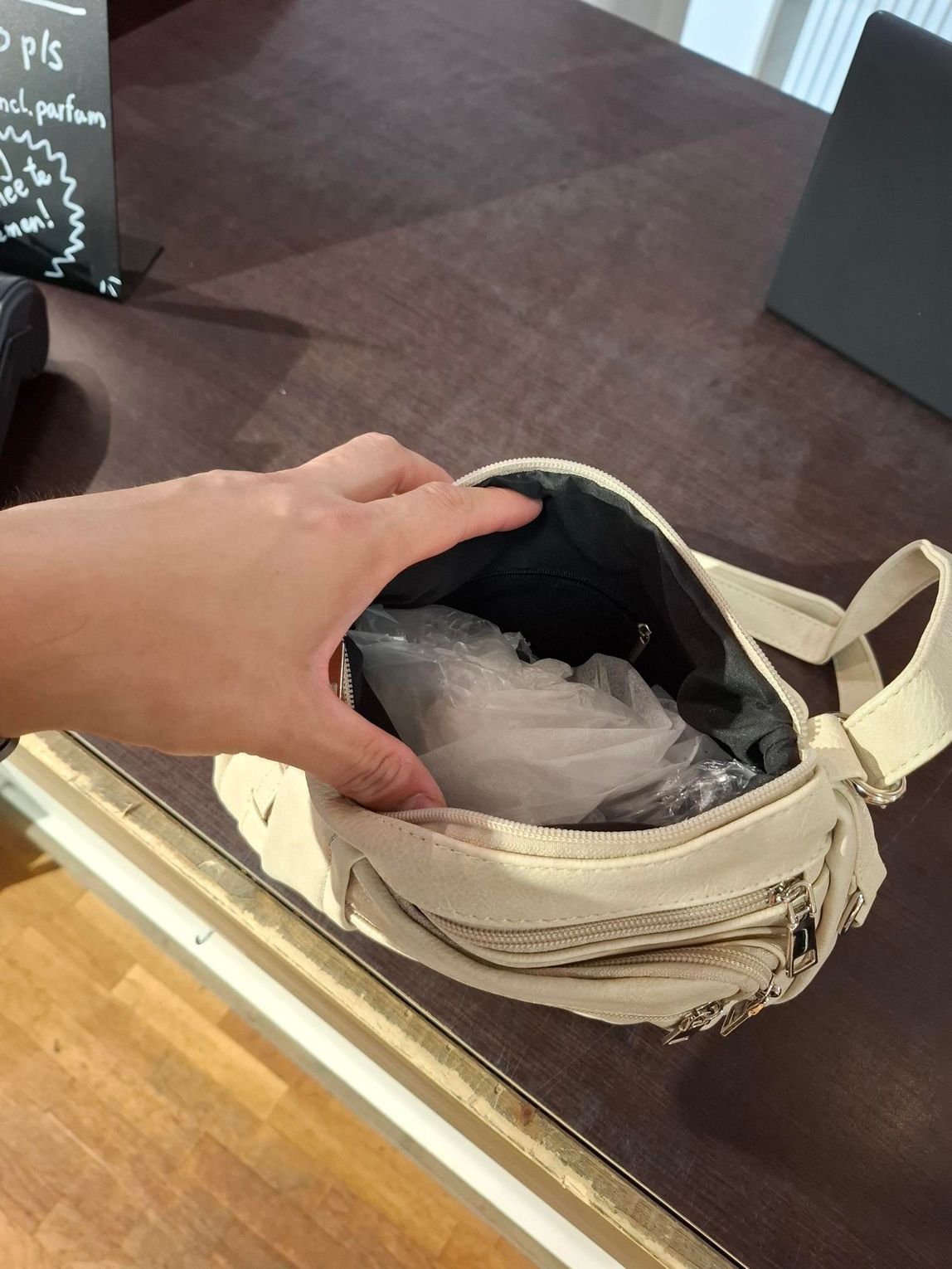 Hand die een zwarte leren schoudertas vasthoudt voor schappen met verpakte accessoires.