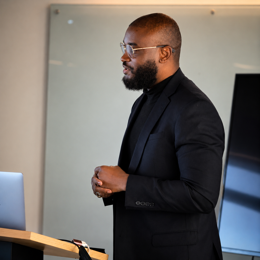 Dr Ola in velvet blazer and turtleneck, seated, looking at camera.