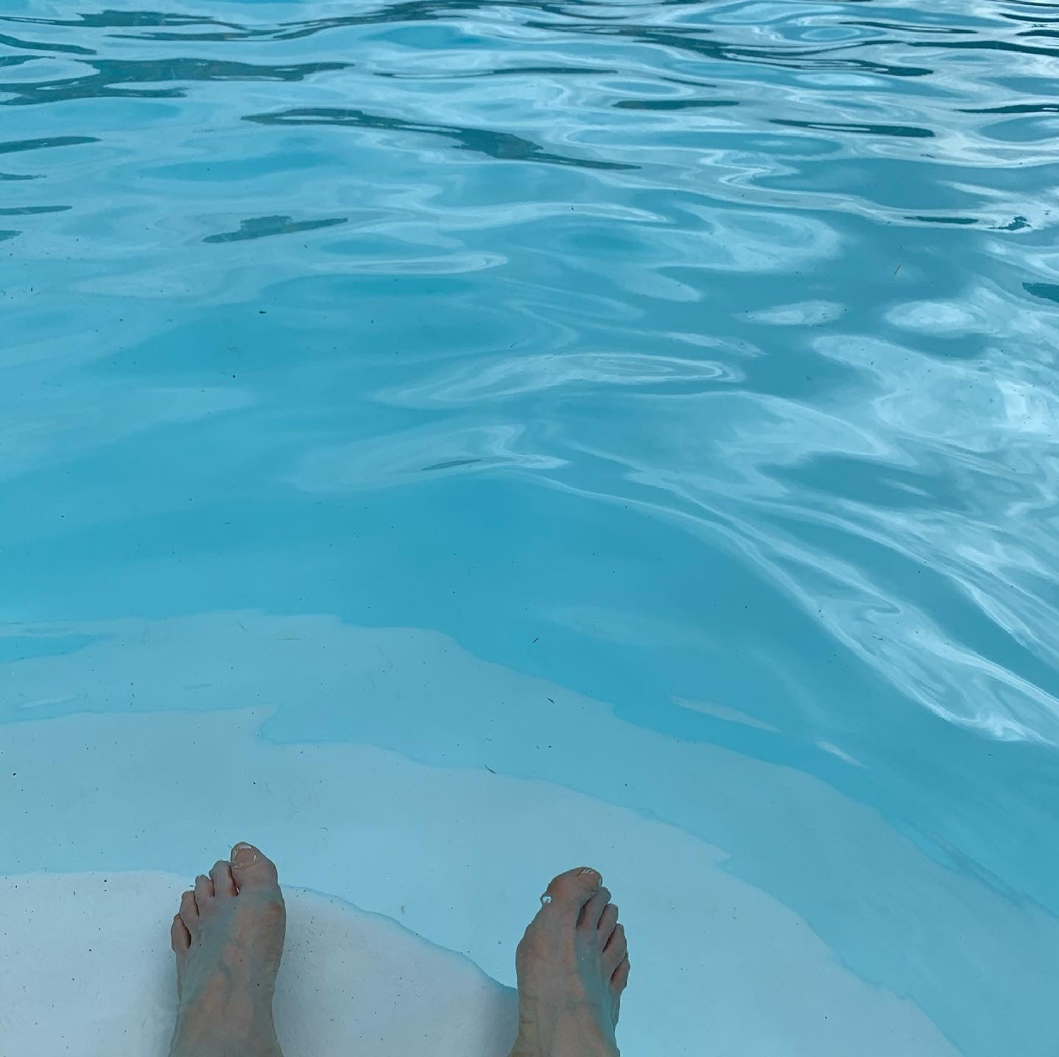 a person 's feet are floating in a swimming pool .
