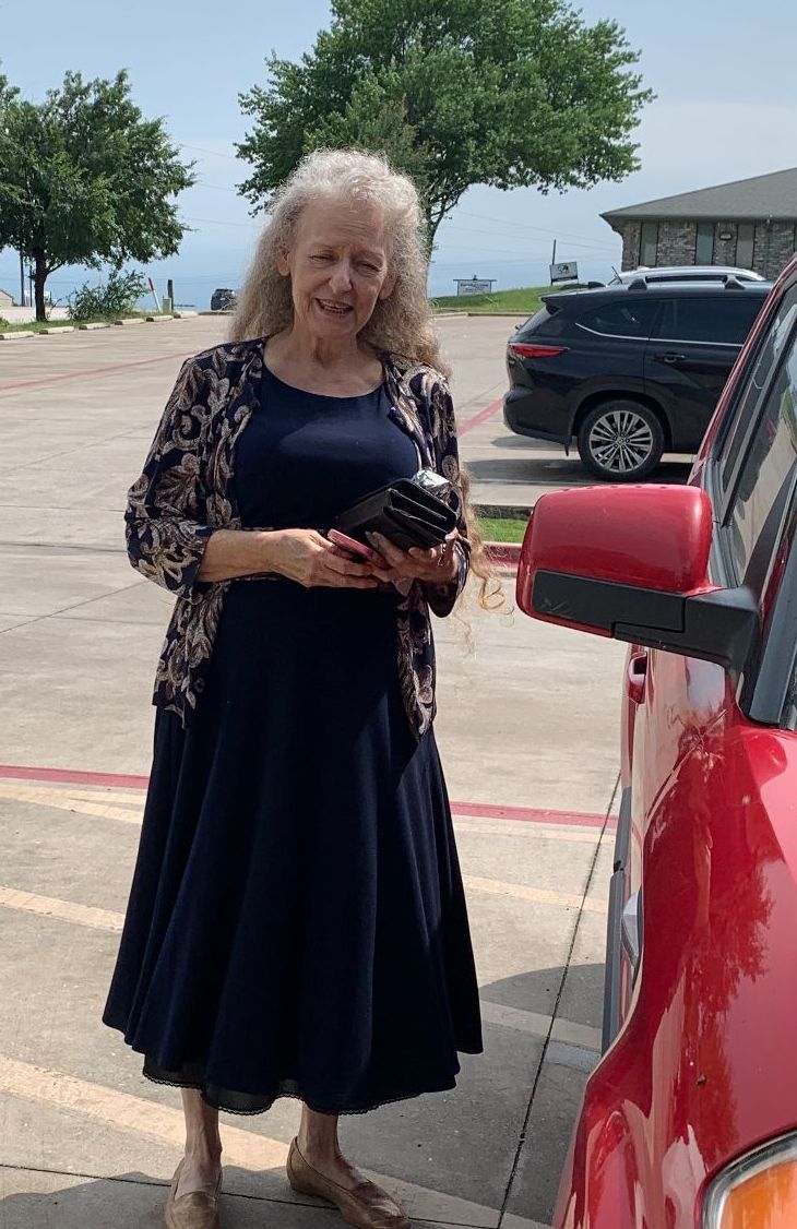 older lady with long hair in a dress standing by vehicle in sunshine