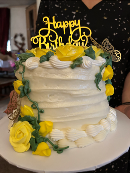 A woman is holding a birthday cake with yellow flowers and a happy birthday topper