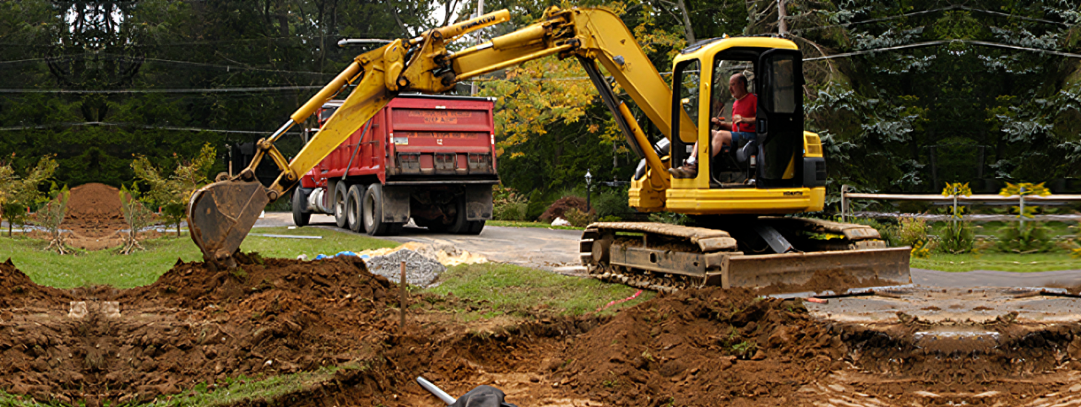 Excavator loading a red dump truck with dirt on a construction site.