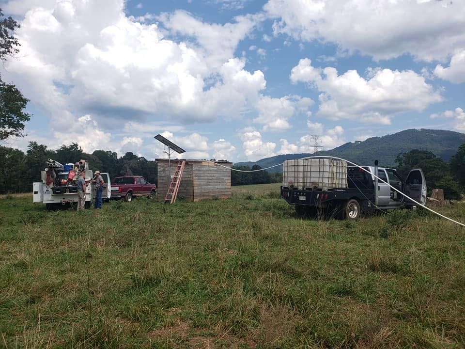 People with trucks and water tanks in a grassy field under a cloudy sky