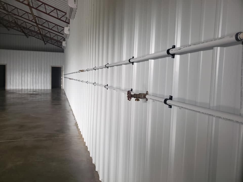 Empty warehouse interior with white corrugated walls and exposed metal pipes along the side.