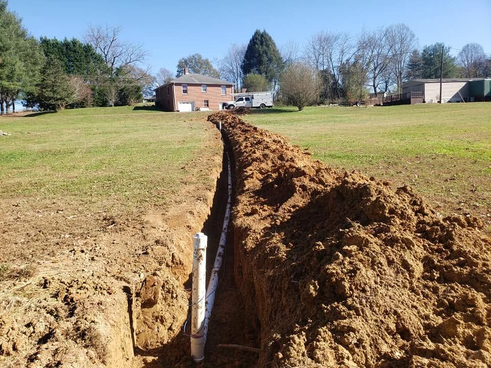 Trench cut through a grassy yard toward a brick house on a sunny day