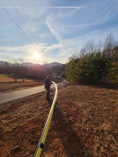 Person holding a long hose on a rural path at sunset, with trees and hills in the background.