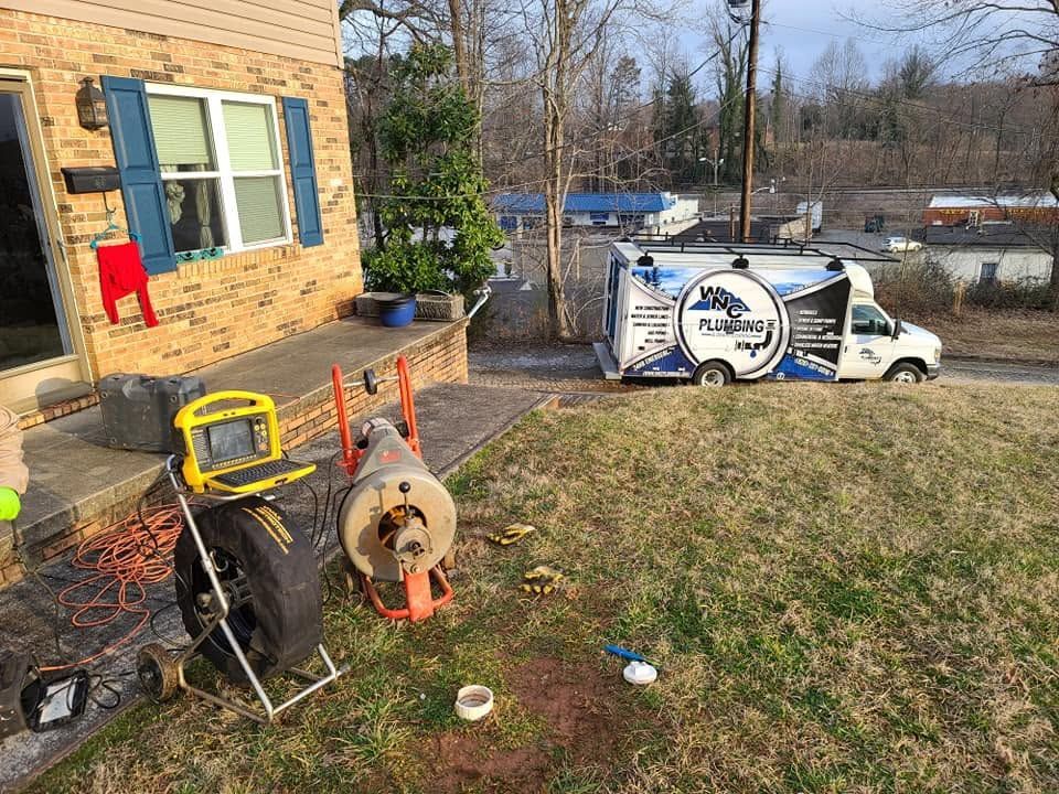 Backyard with utility trailer, hose reel, and brick house beside a grassy yard and river.