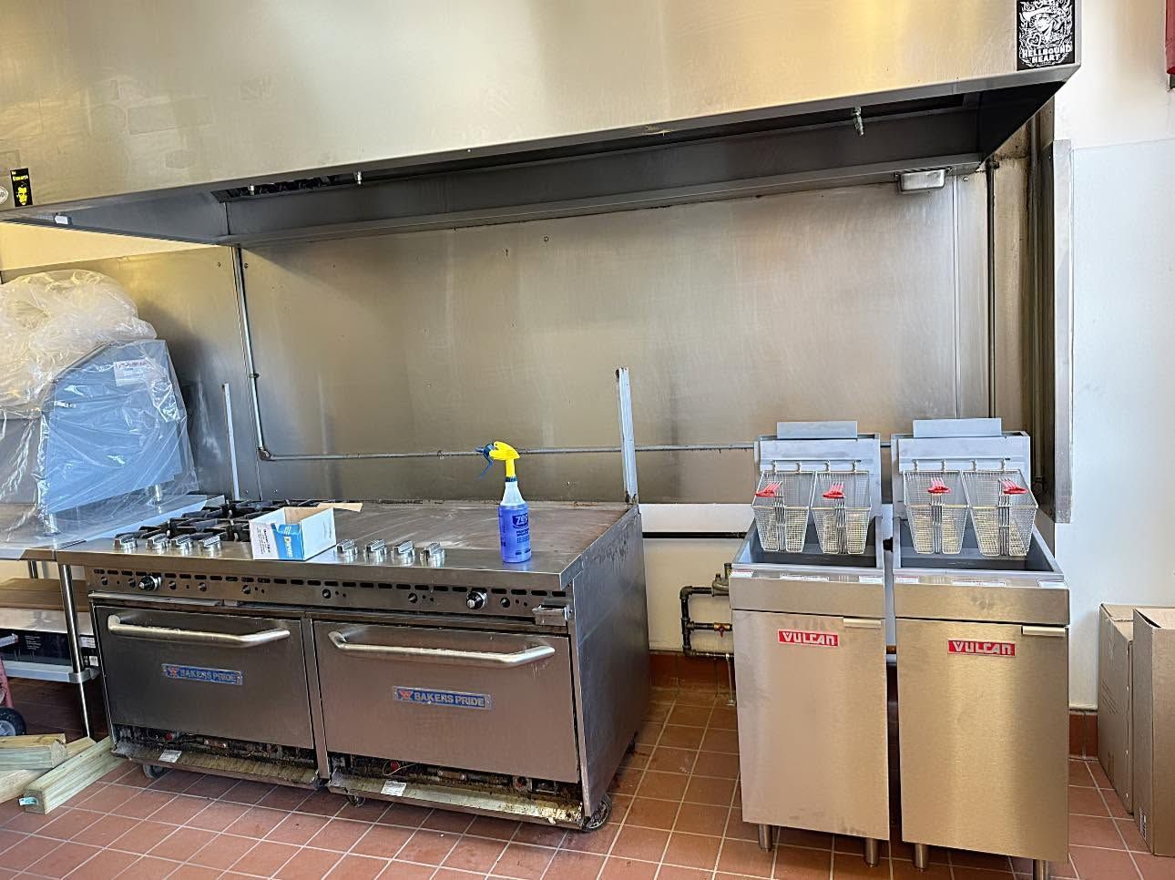 Commercial kitchen prep area with stainless steel counters, sinks, dish racks, and a tiled wall