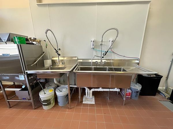 Stainless steel double sink and prep area in a commercial kitchen with buckets and shelves underneath