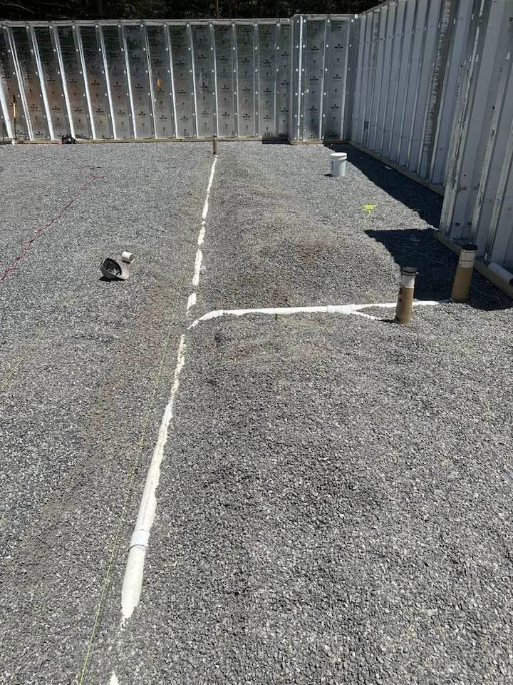 Gravel rooftop with HVAC vents and a white painted line beside a gray wall