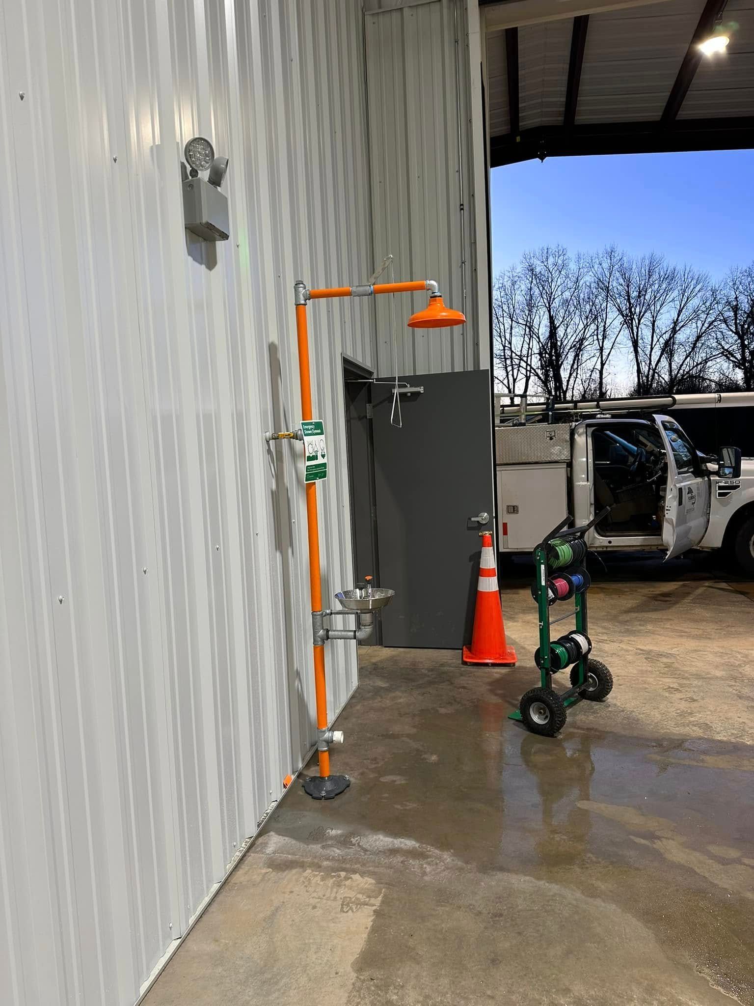 Outdoor utility area beside a striped wall with safety cones, a mounted light, and a work cart near a vehicle.