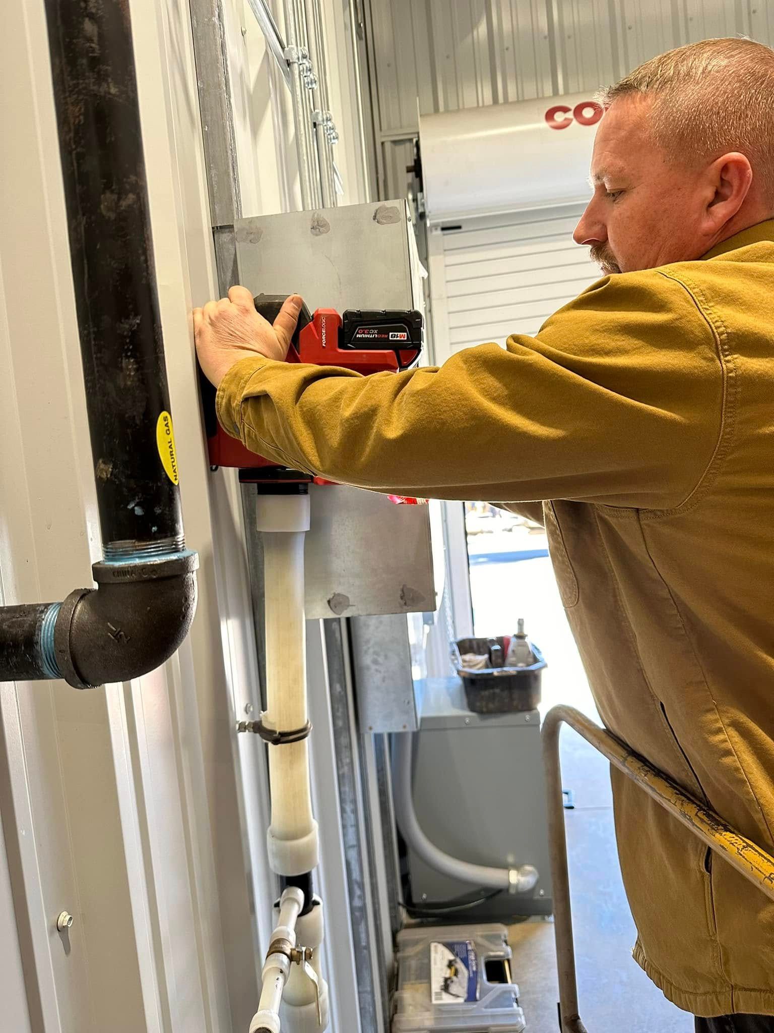 Person in a mustard jacket adjusting a red device on a gray utility system indoors.
