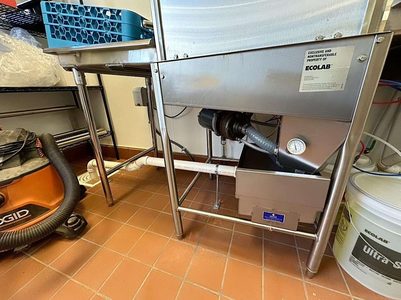 Metal worktable in a kitchen area with a white basin, hose, and stacked buckets on tiled floor.