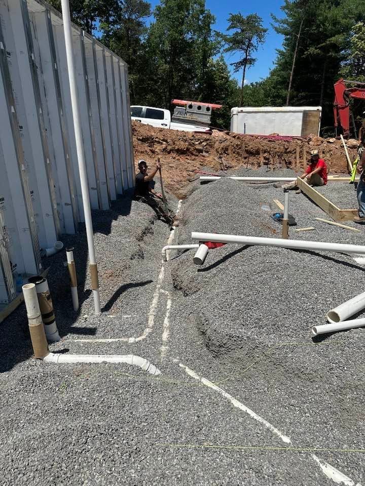 Construction site with workers laying white pipes beside a gravel trench and white metal wall panels.