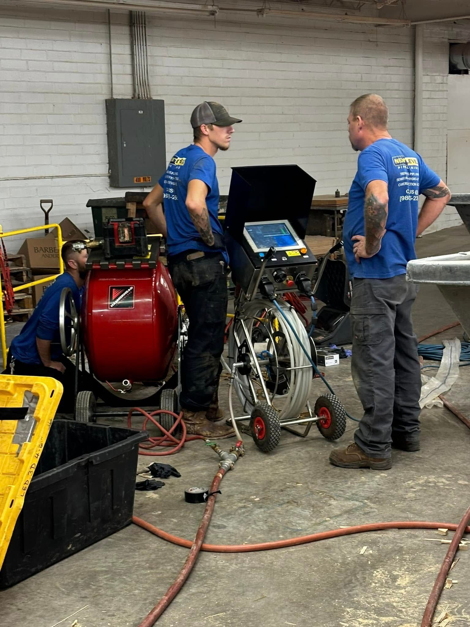 Two mechanics in blue shirts inspect equipment in a workshop beside a red air compressor.