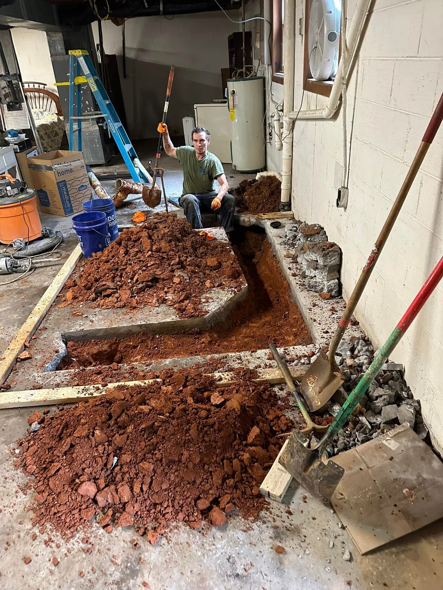 Flood-damaged room with piles of wet red debris, a shallow trench, and cleaning tools along the wall