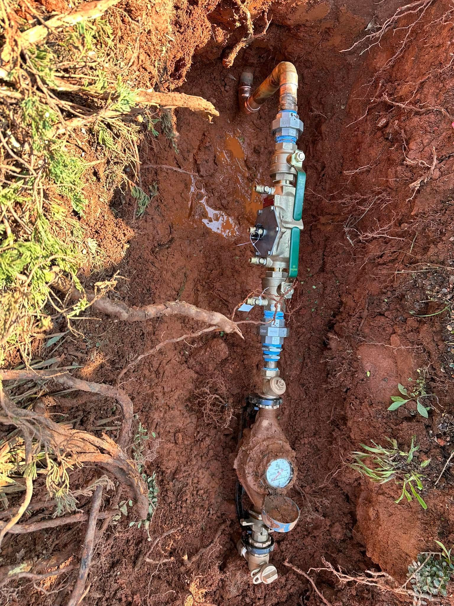 Exposed underground pipe with blue valves in a dirt trench