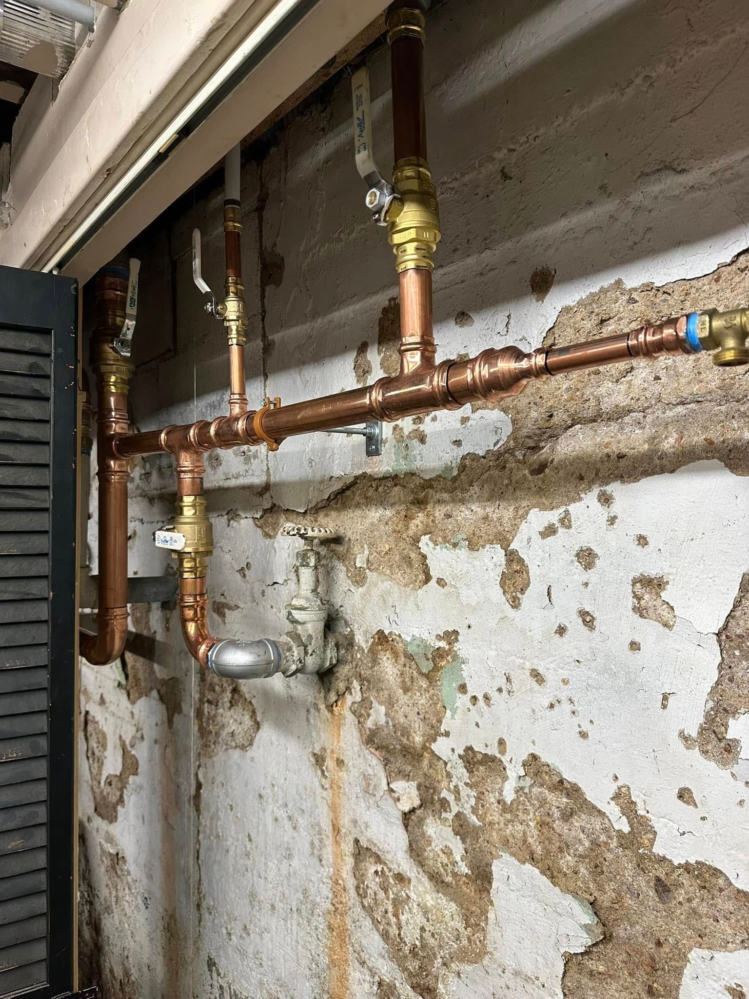 Copper pipes and valve assembly running along a basement wall with peeling paint and concrete stains