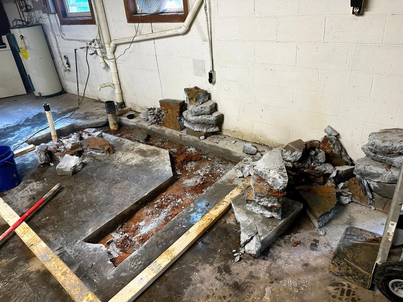 Flood-damaged basement with muddy water, broken floor, and exposed pipes and debris