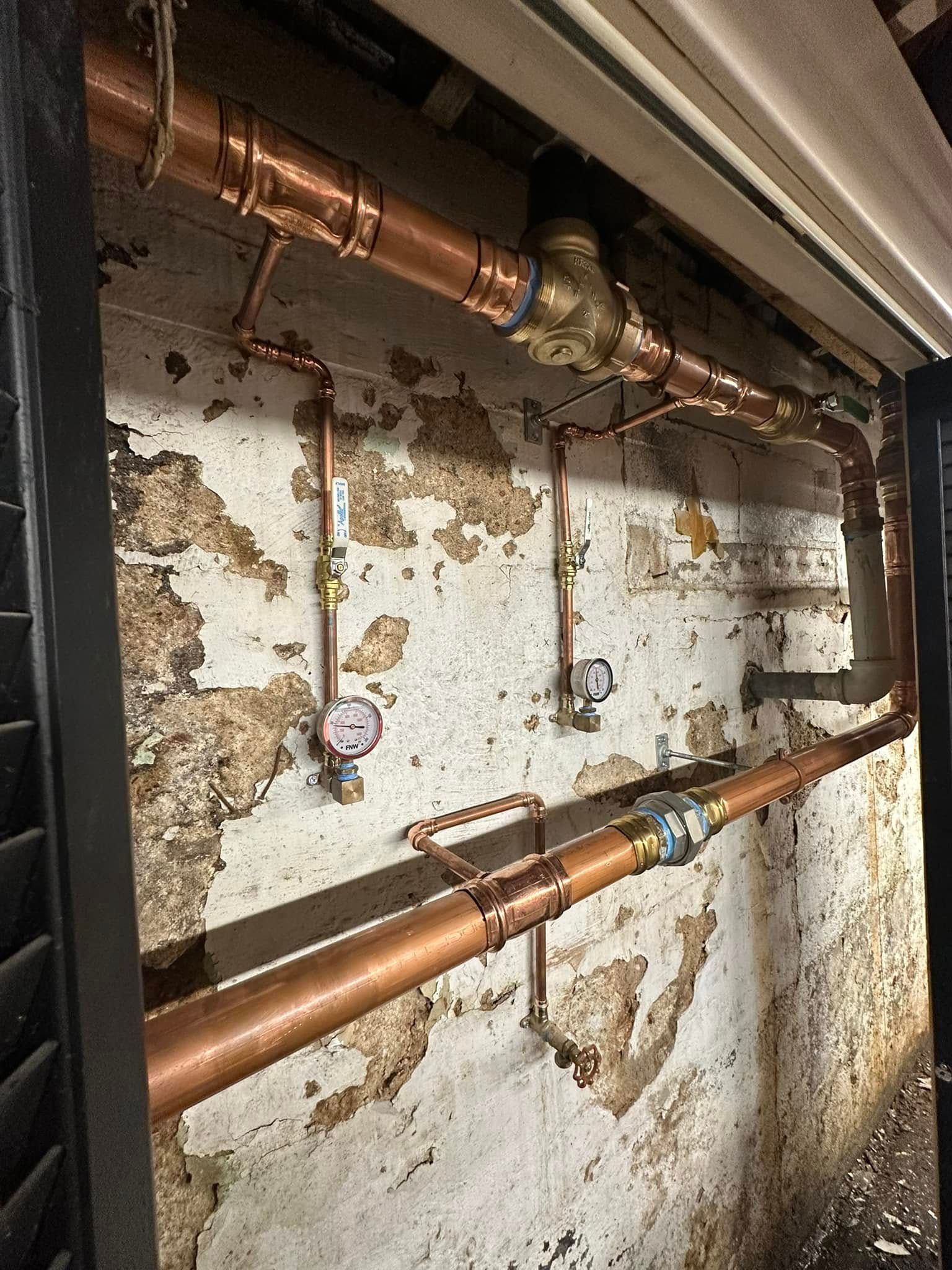 Corroded copper pipes running along a peeling basement wall with water damage and exposed plaster