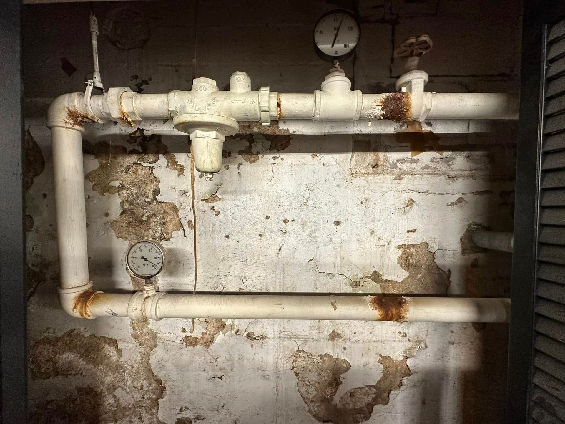 Rusty pipes and gauge on a stained industrial wall.
