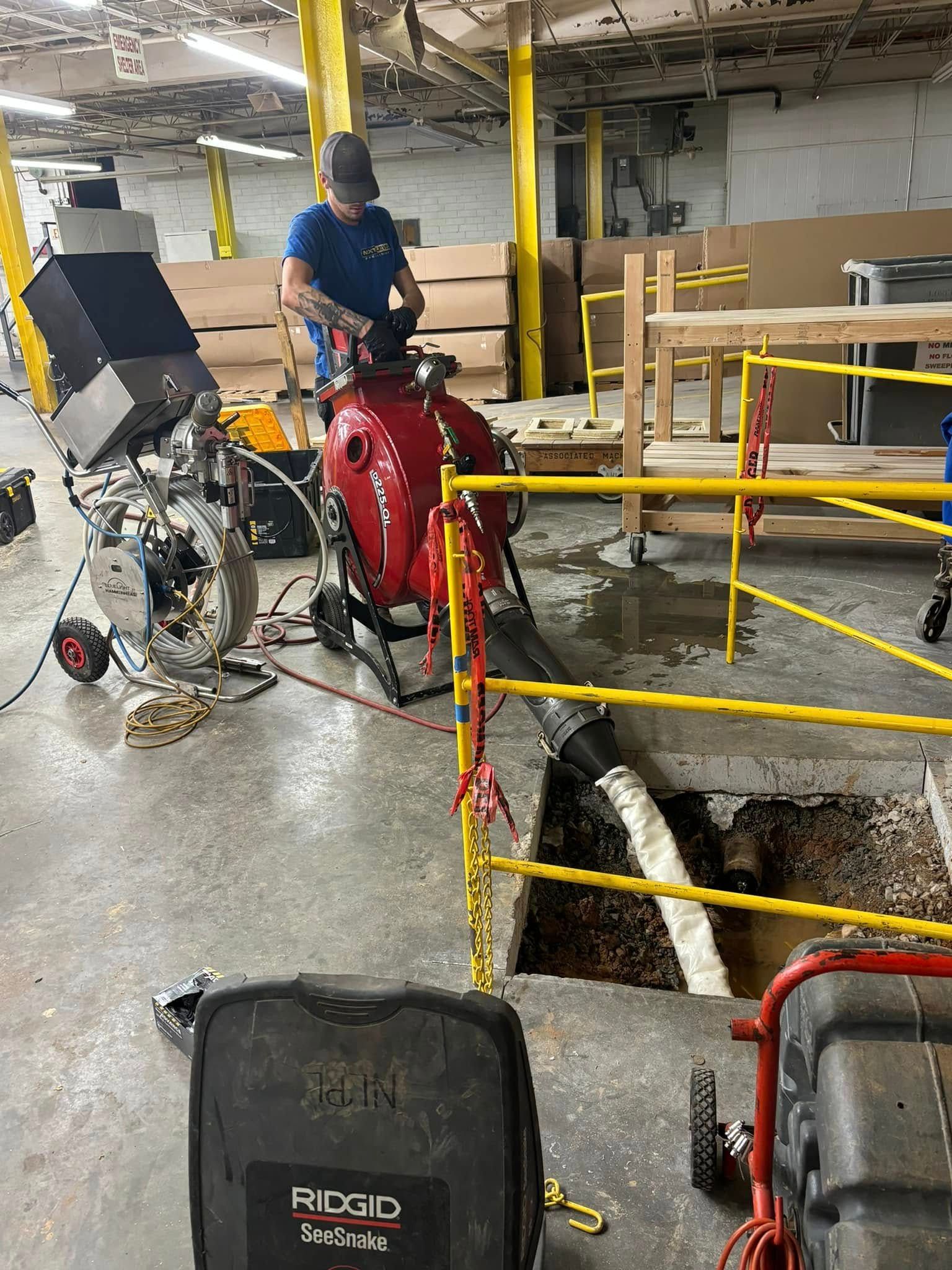 Worker operating red machinery beside a trench in an industrial basement area