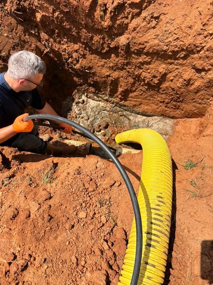 Worker using a hose and yellow corrugated pipe in a rocky excavation site