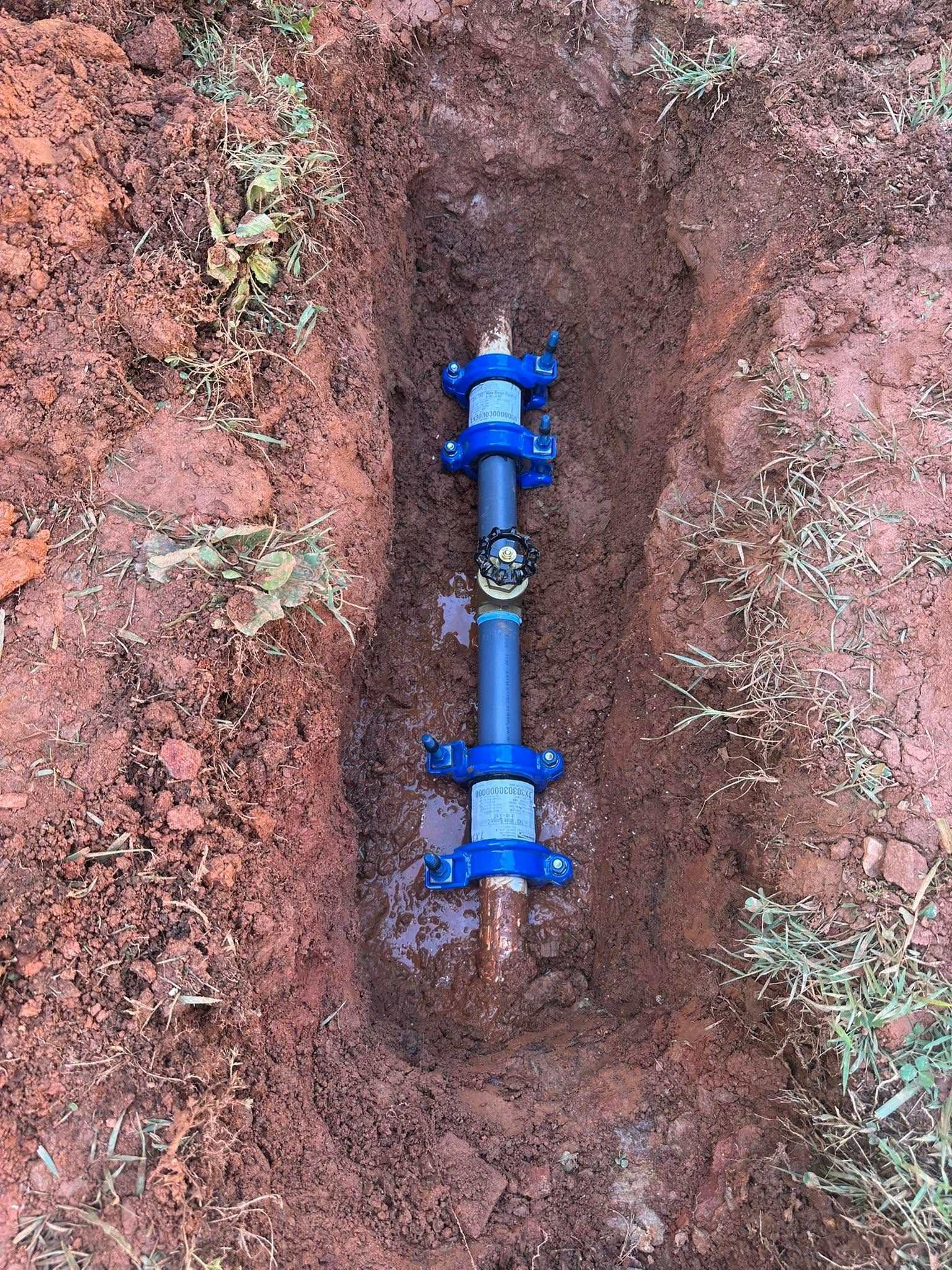 Blue pipe valve assembly installed in a narrow trench of reddish soil
