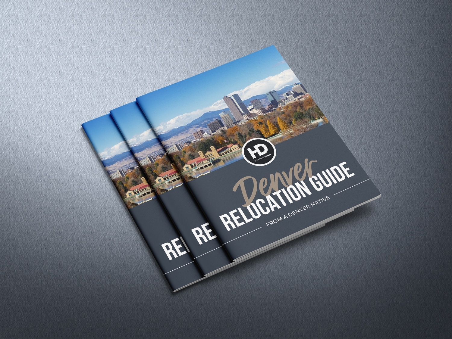 Three blue “Denver Relocation Guide” booklets fanned on a gray surface
