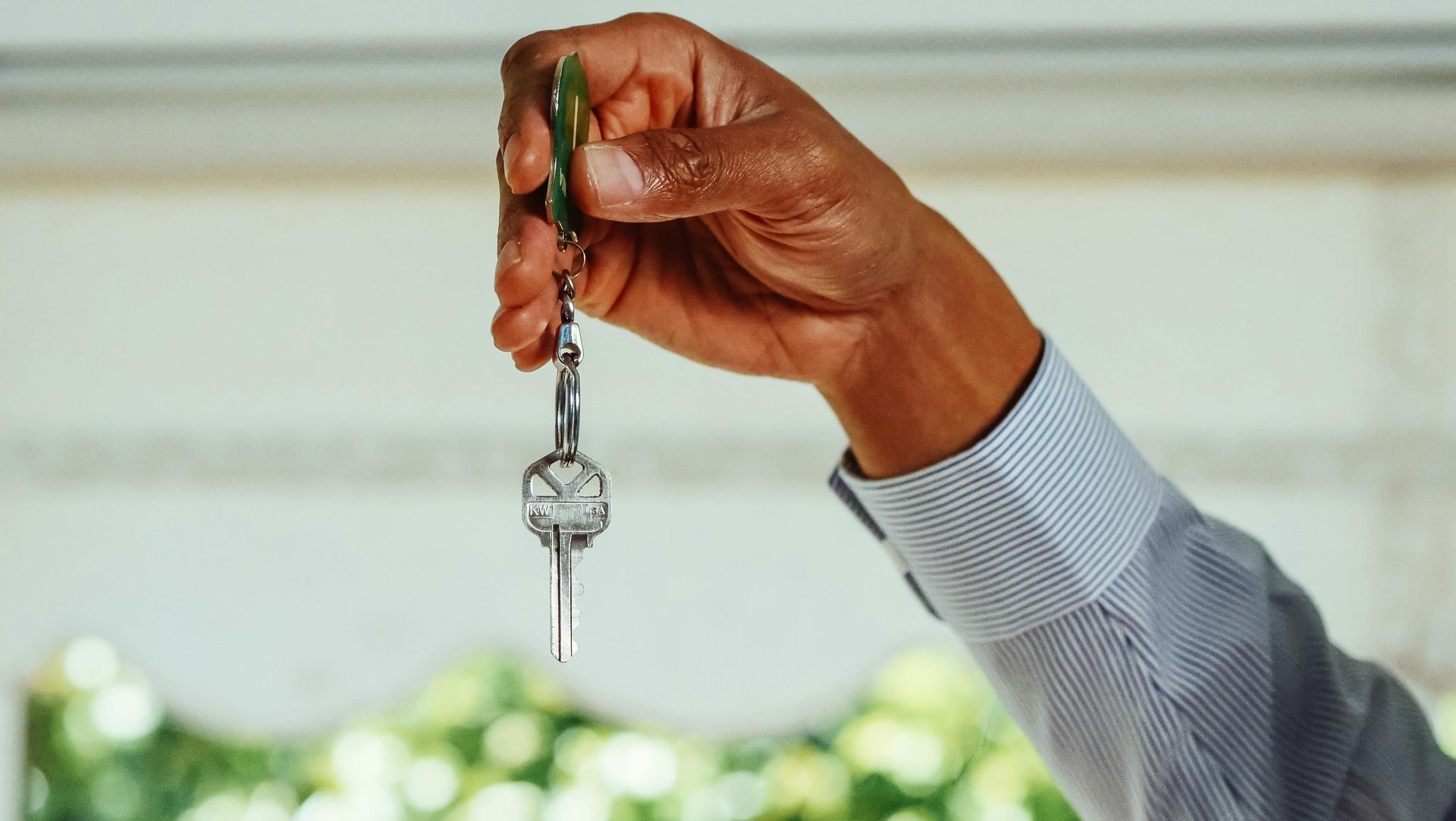 Hand holding a key with green tag against a blurred indoor background