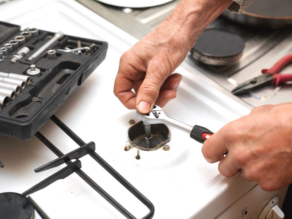 A man is fixing a stove with a wrench and pliers