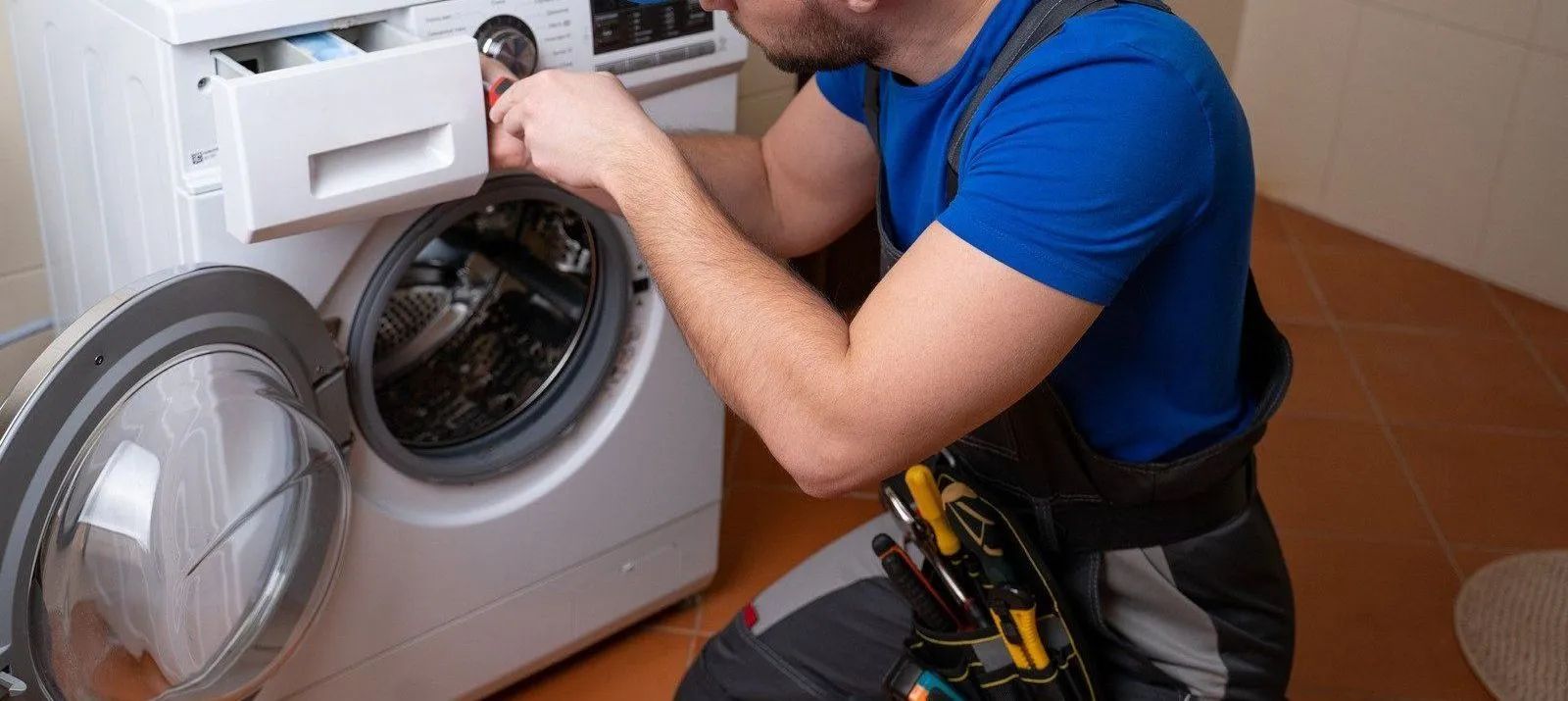 Technician repairing a front-loading washing machine in a laundry room
