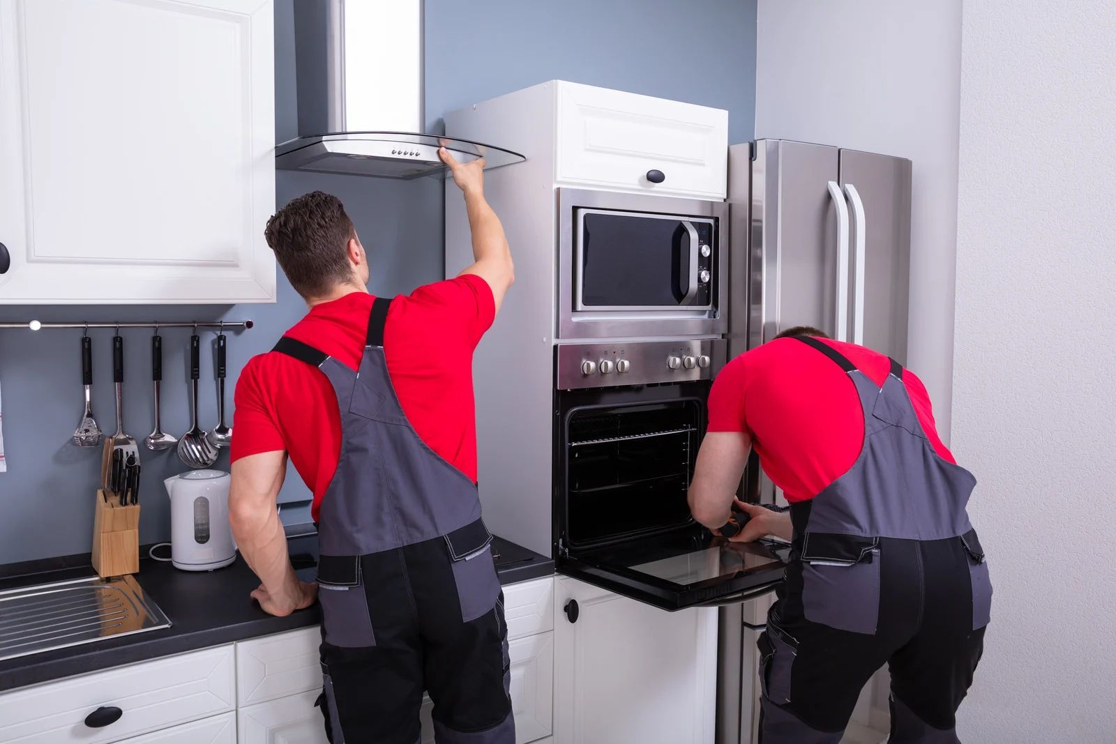 Two technicians in red shirts installing a stainless steel oven in a modern kitchen