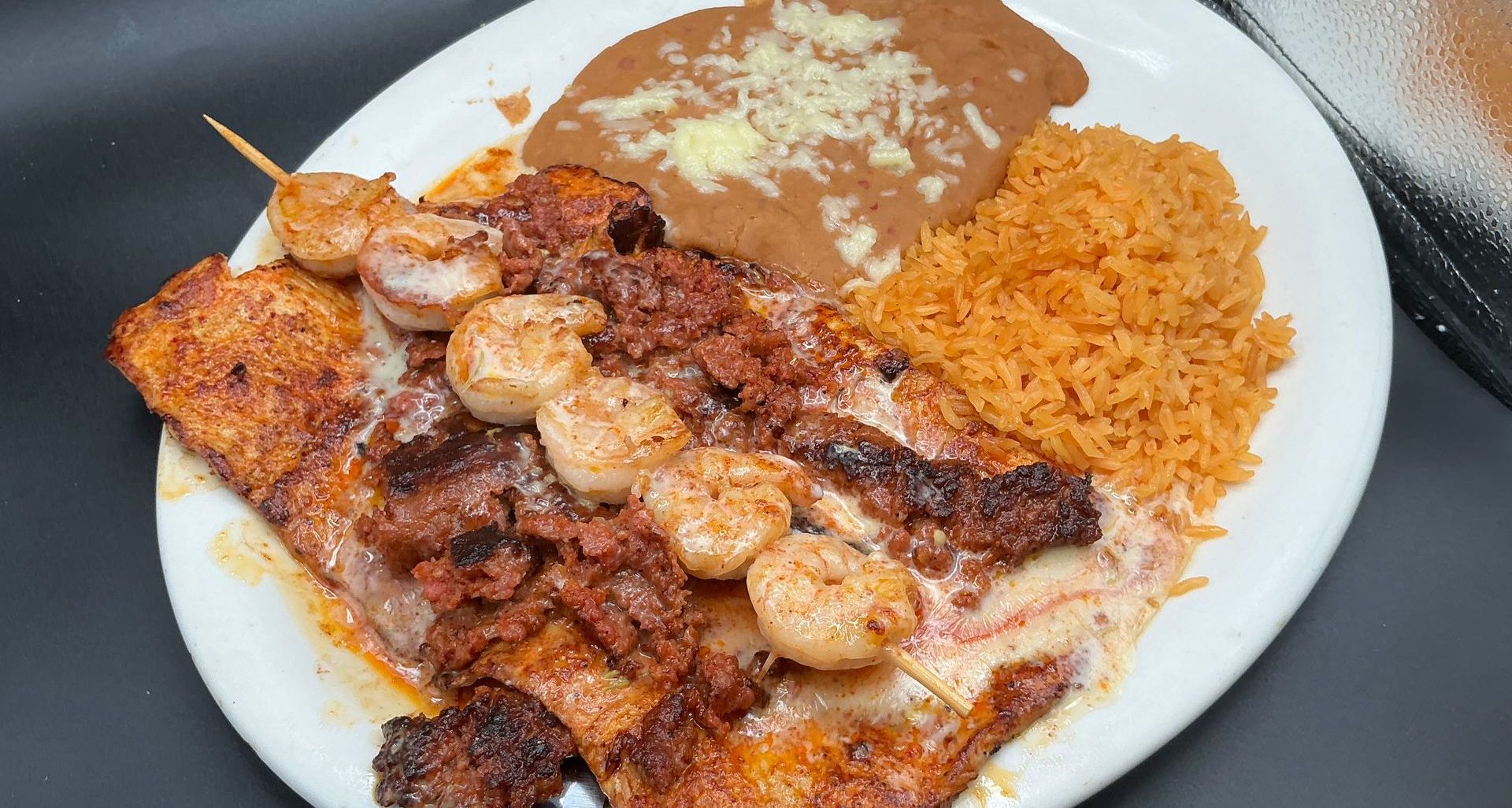 Plate of food with grilled seafood, rice, and refried beans.