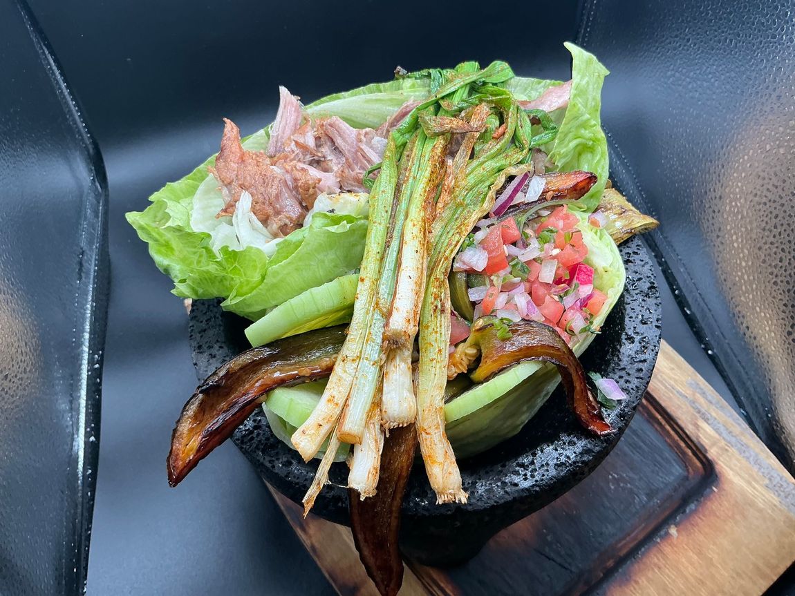 Taco salad with grilled onions, salsa, and lettuce served in a stone bowl on a wooden board.