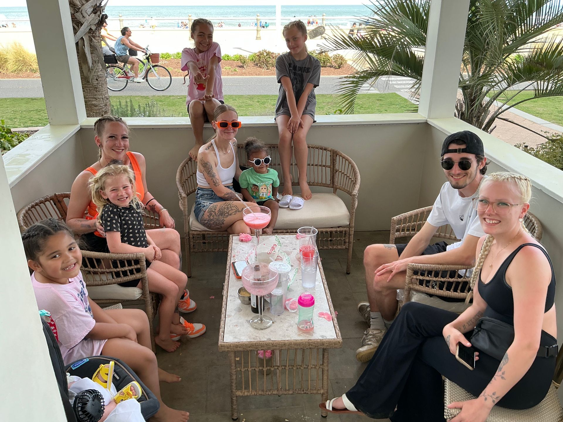 Group of people on a patio with a beach view, seated around a table with drinks.