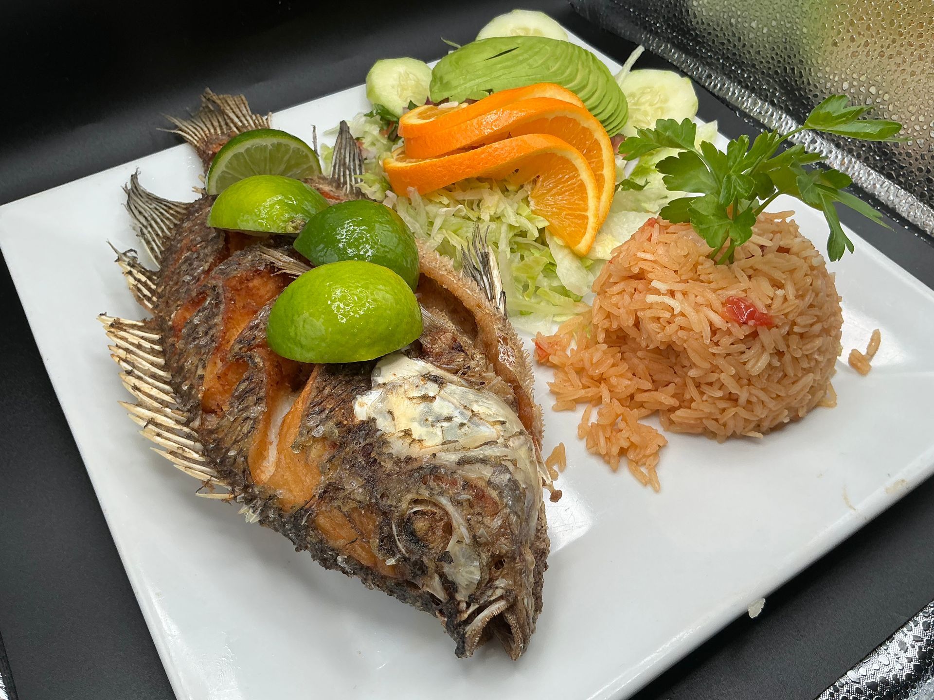 Fried fish with lime wedges, rice, and salad on a white plate.