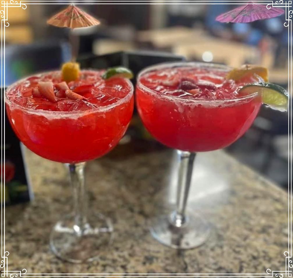 Two strawberry margaritas in stemmed glasses, garnished with fruit and umbrellas on a table.
