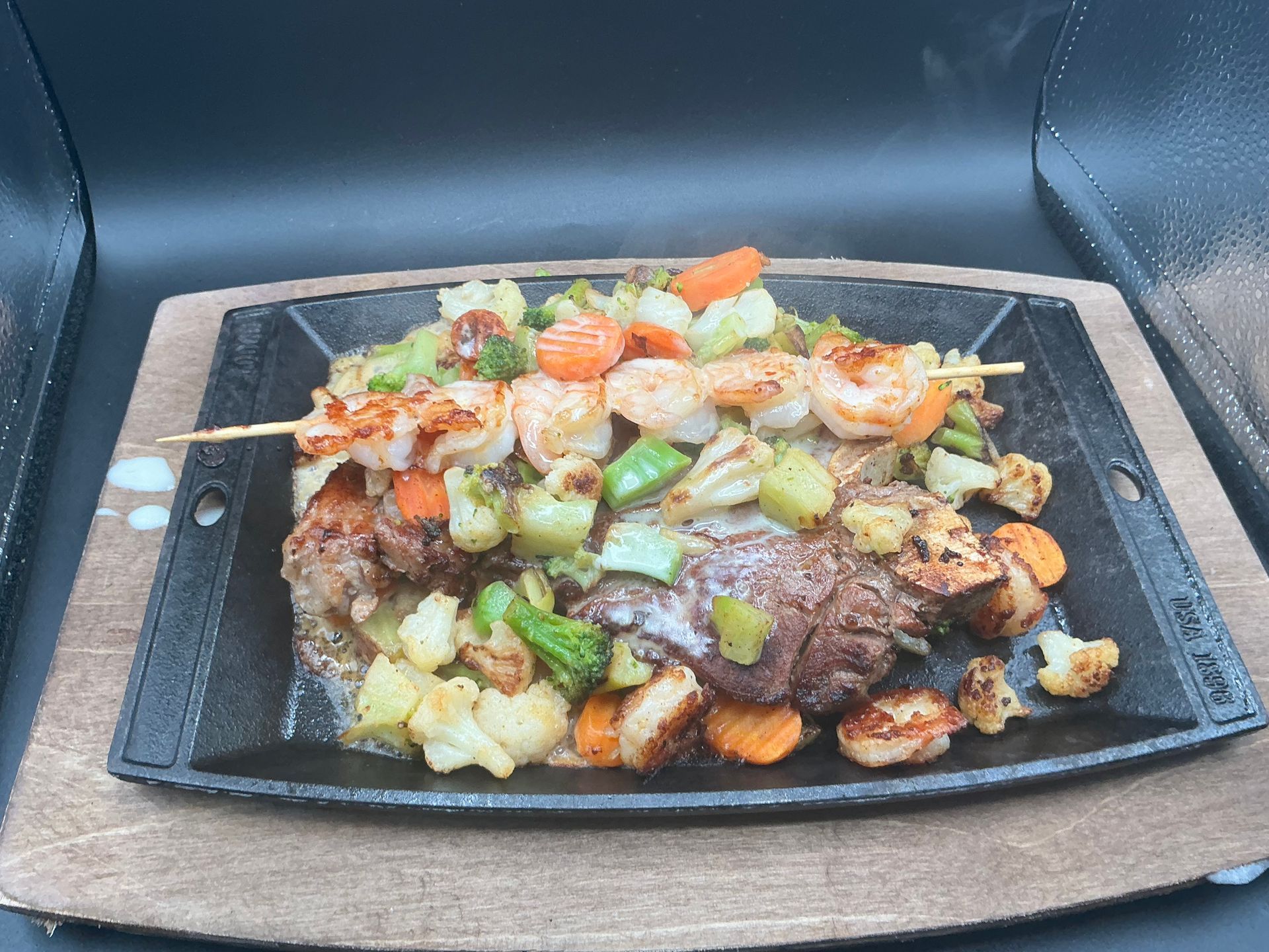 Sizzling platter with steak, shrimp skewer, and roasted vegetables.