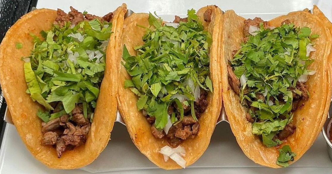 Three golden-brown tacos filled with meat, white onions, and cilantro.