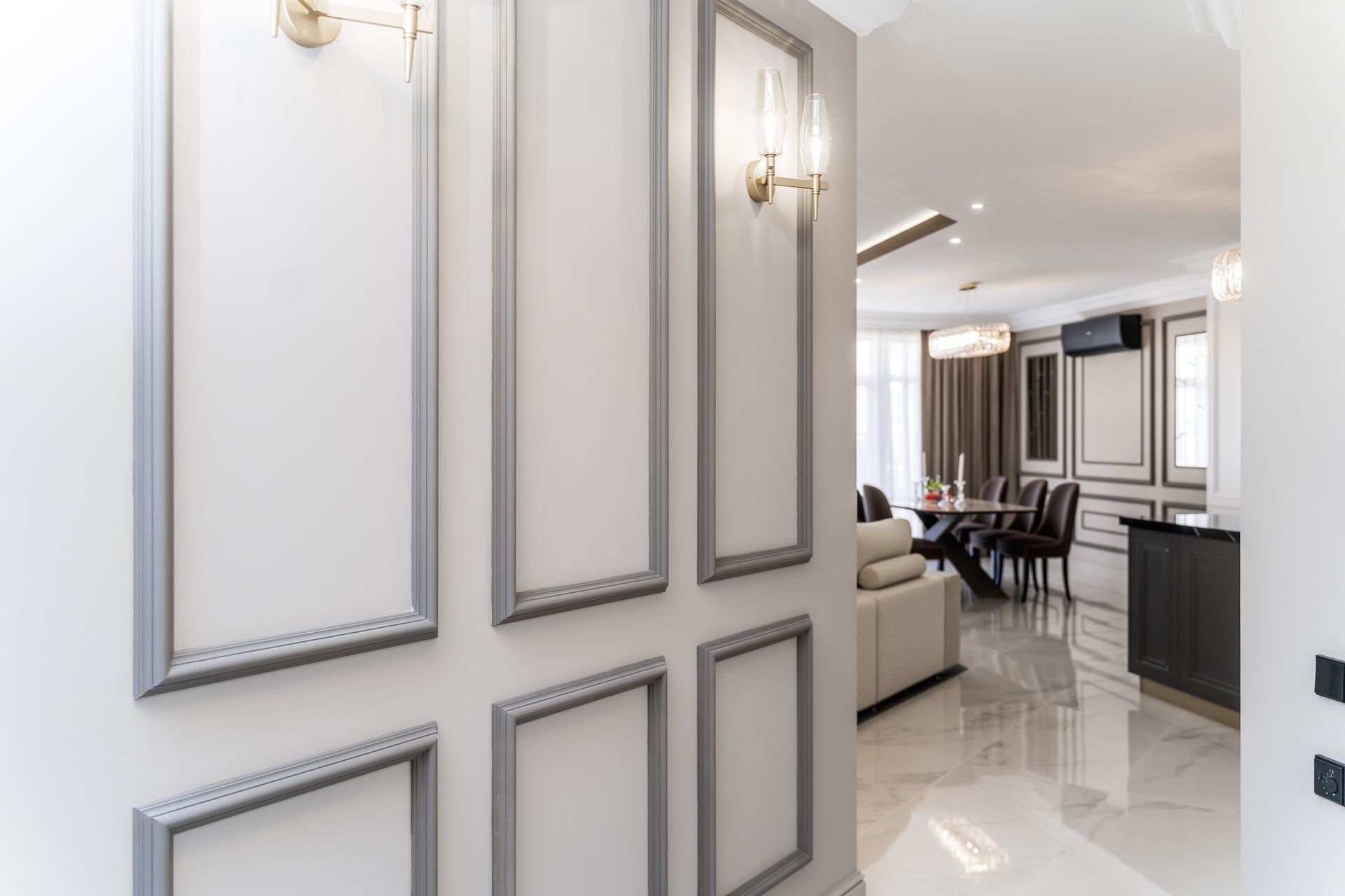 Hallway with white walls, silver trim, and gold sconces, leading to a dining area.
